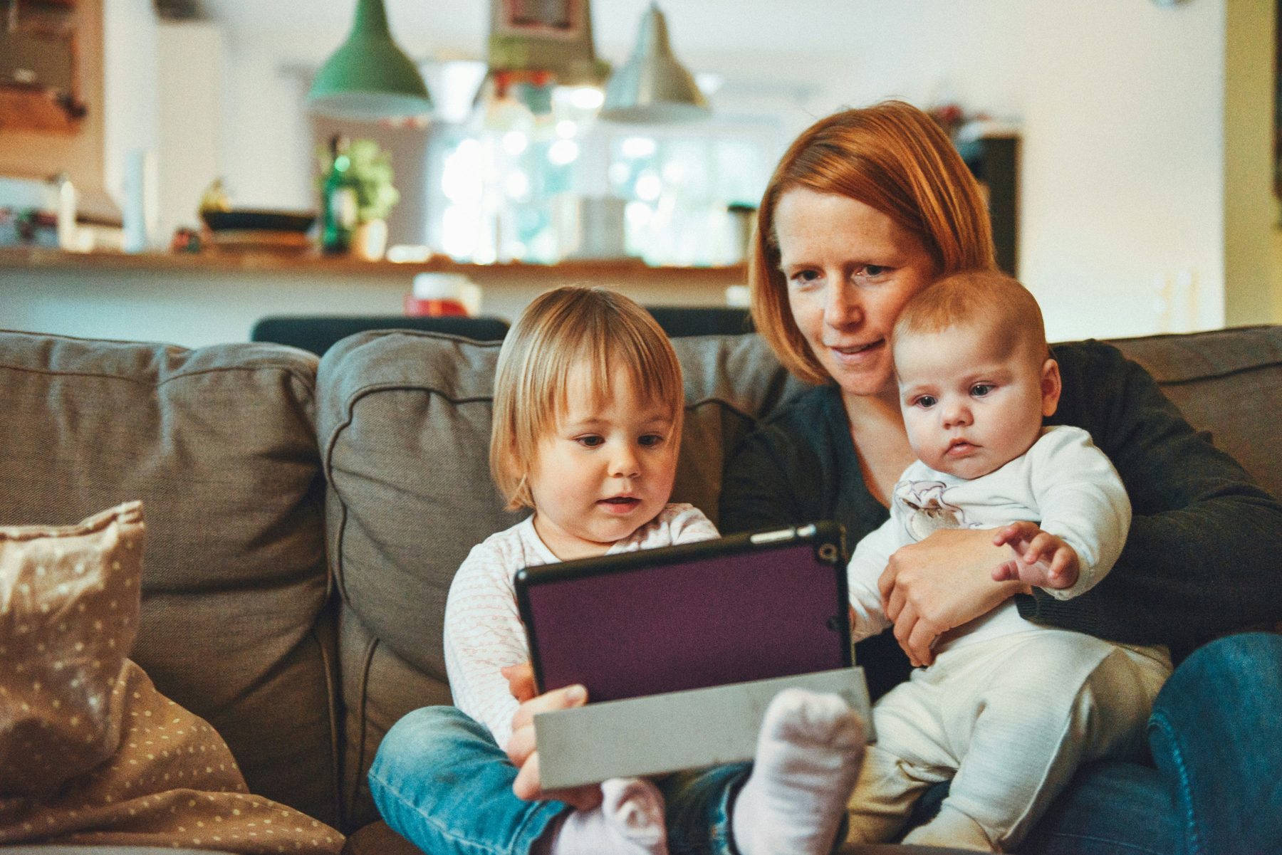 En vuxen i soffan hemma med två små barn